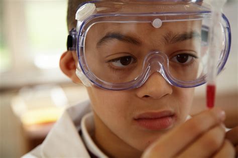 Schoolboy wearing protective goggles holding up pipette 